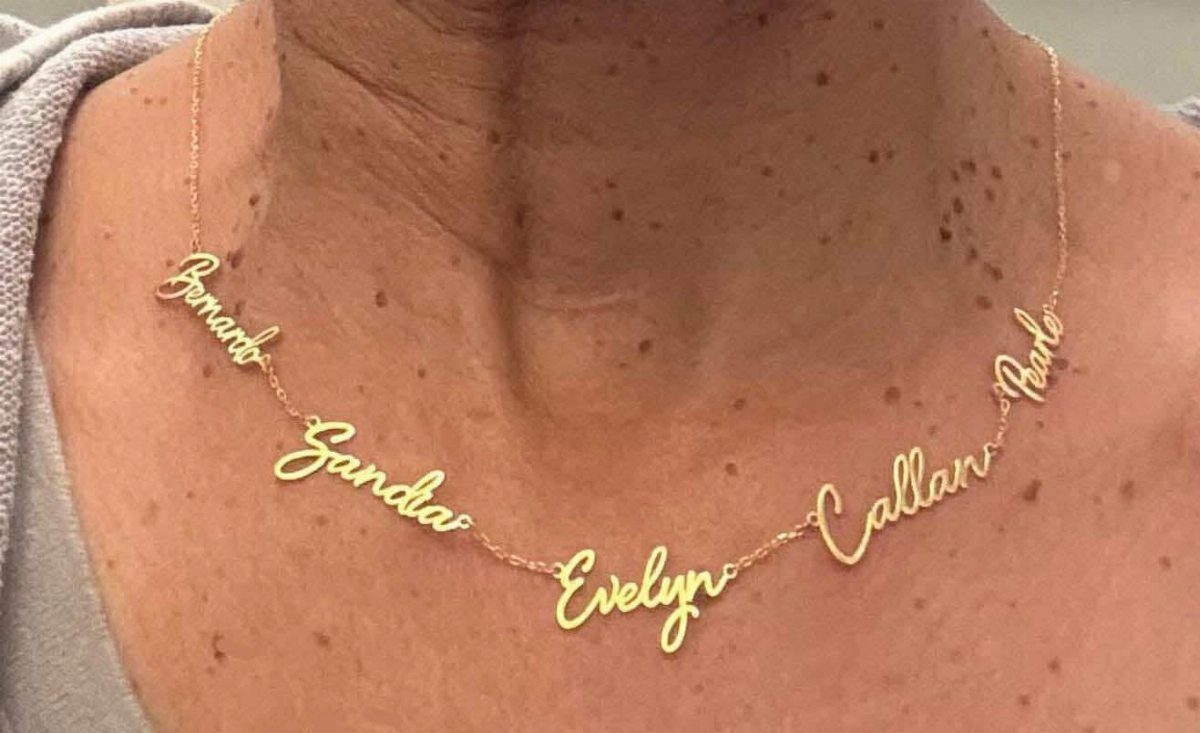 Gold personalized name necklace with five cursive names worn around a person's neck.