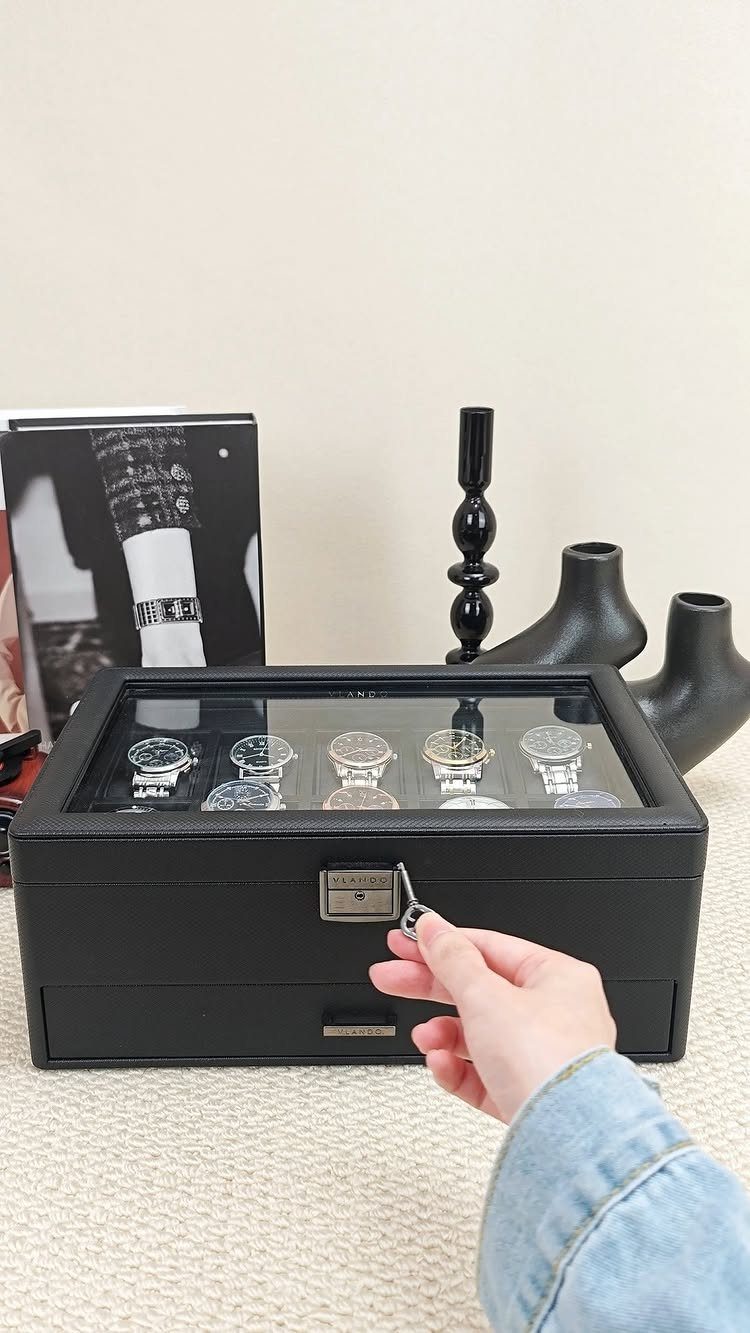 Black leather watch box with five silver watches being unlocked by a hand.