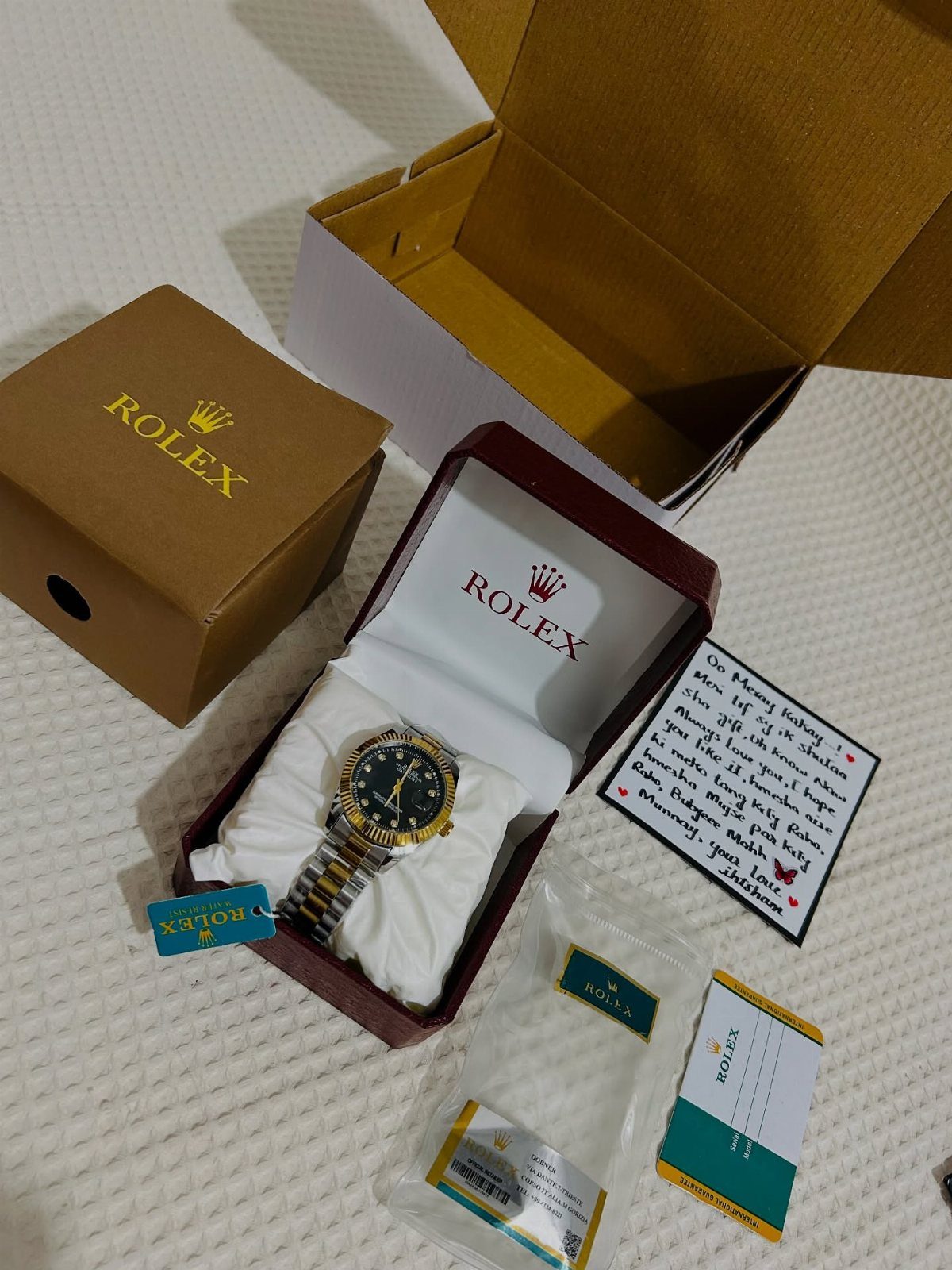 Rolex watch in a maroon box with a birthday card and packaging.