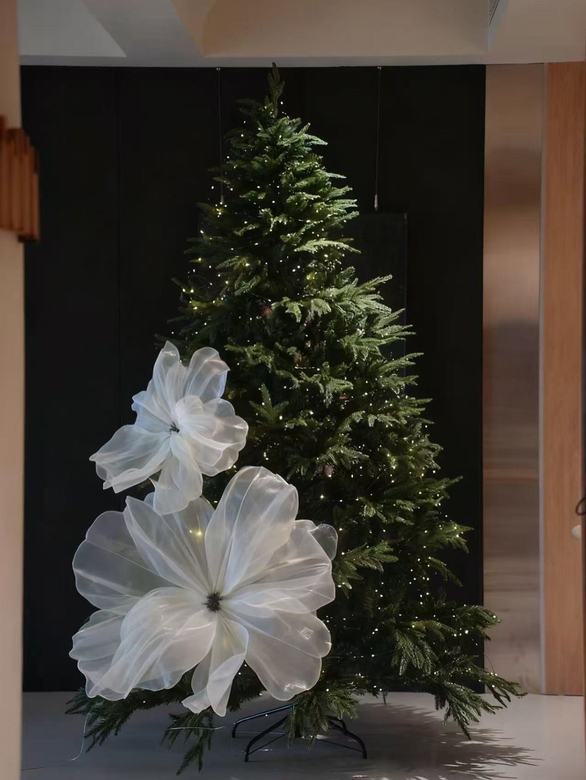 Green Christmas tree with warm white lights and large white fabric flowers.