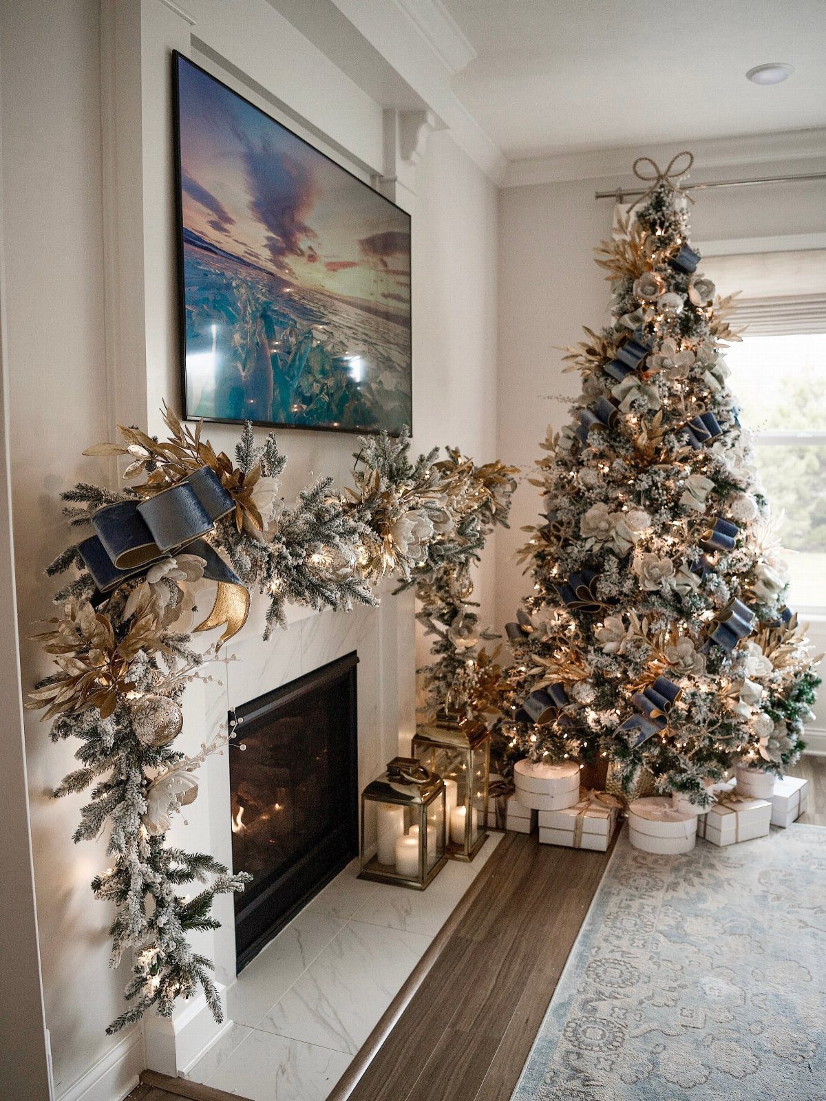 Flocked white Christmas tree with gold and navy decorations next to a fireplace.