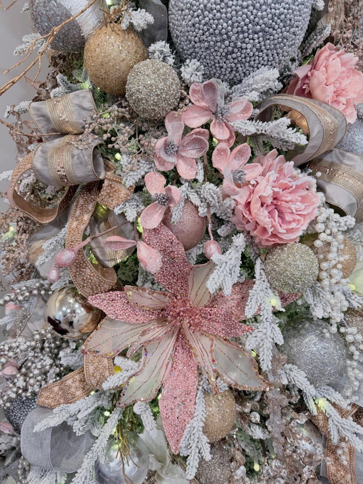 White flocked Christmas tree decorated with pink flowers, gold and silver glittery ornaments.