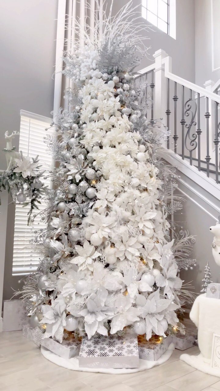 Flocked white Christmas tree decorated with silver ornaments and white poinsettia flowers.