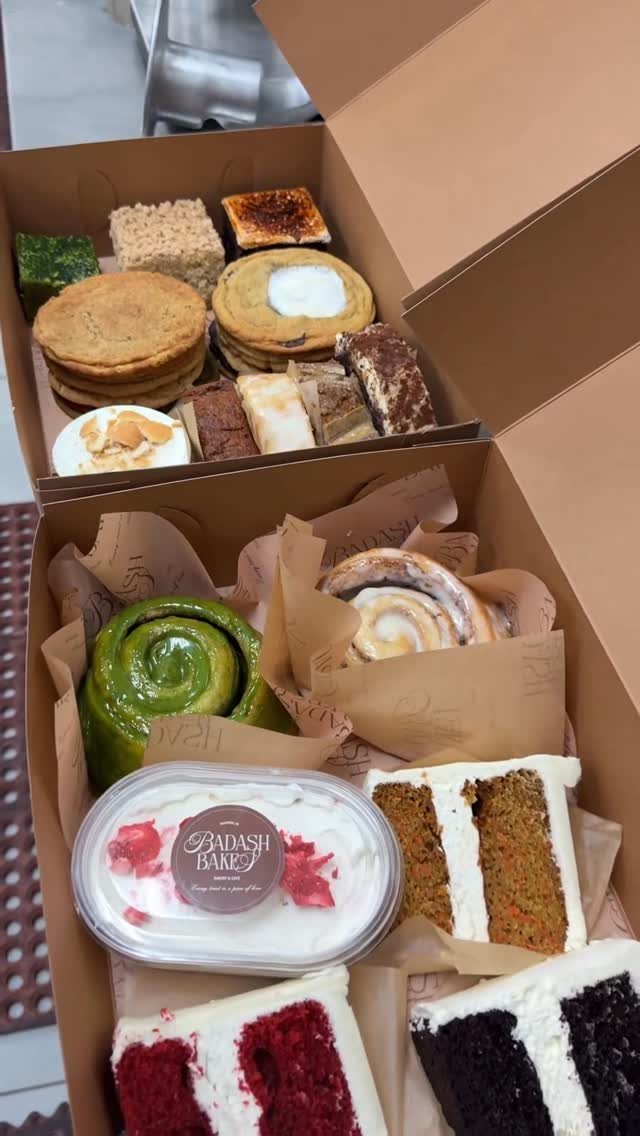 Assorted baked goods and cakes in two open brown cardboard delivery boxes.
