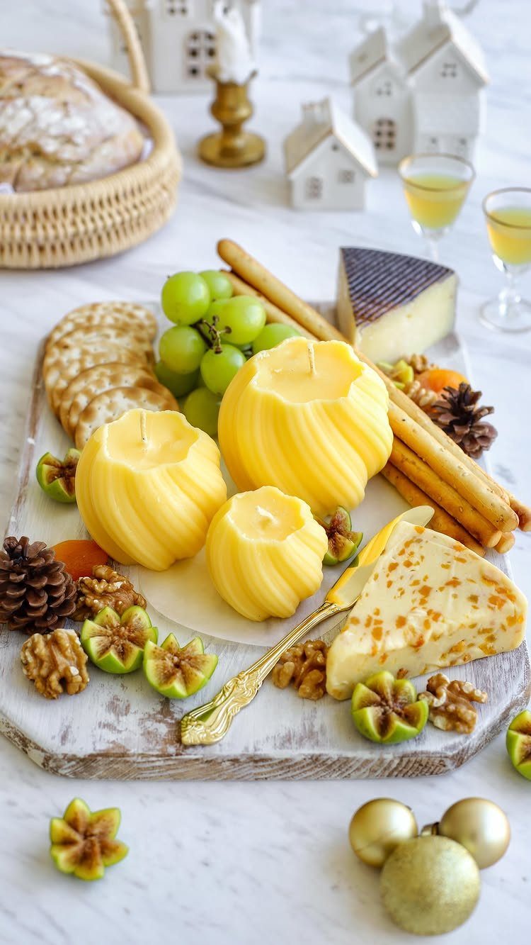 Cheese-shaped yellow candles on a charcuterie board with grapes, nuts, and cheese.