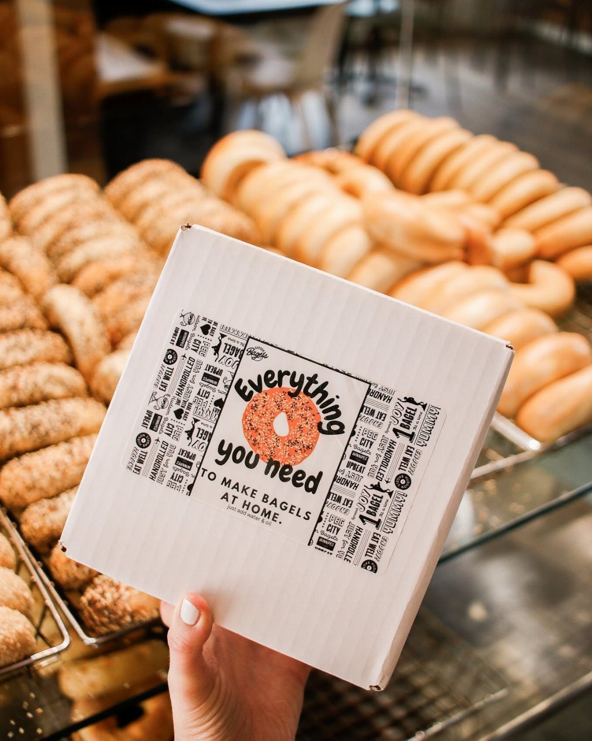 Bagel making kit box held in front of fresh bagels in a bakery