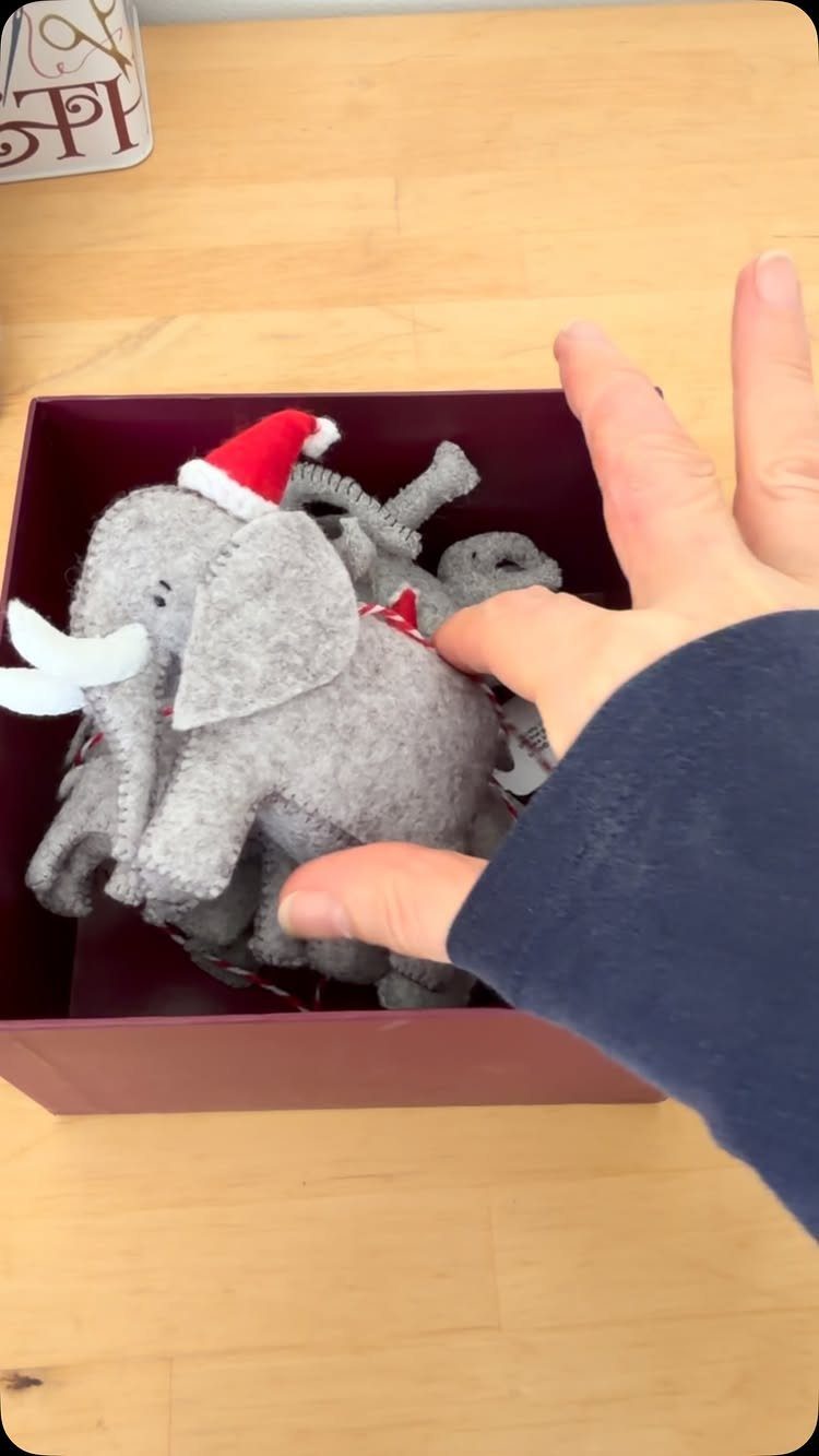 Grey felt elephant plushies with a Santa hat inside a maroon gift box.