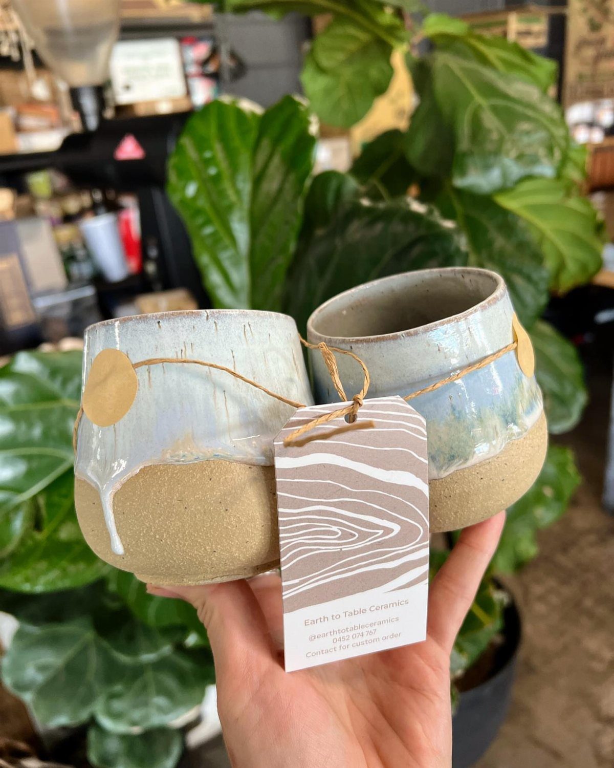 Two handmade ceramic cups tied with twine and a tag held by a hand.