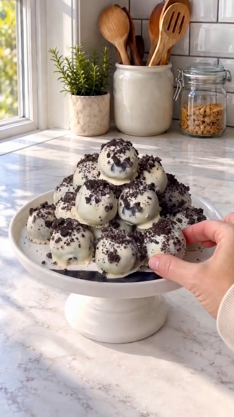 White chocolate cake pops with cookie crumbs on a white pedestal cake stand.