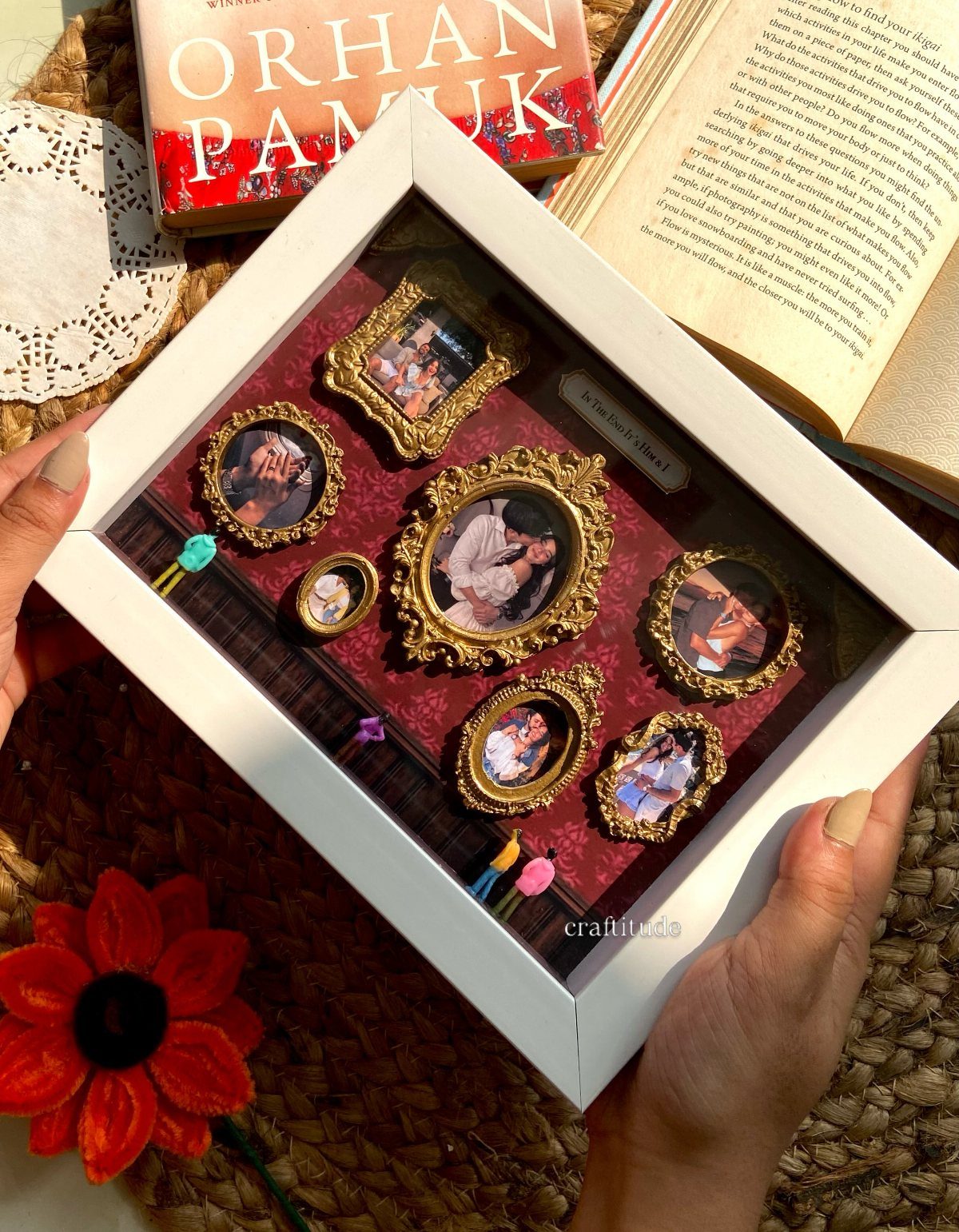 White shadow box containing multiple small gold frames with photos on red velvet.