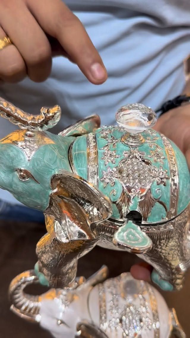 Decorative turquoise and gold elephant trinket box held by a person's hand.