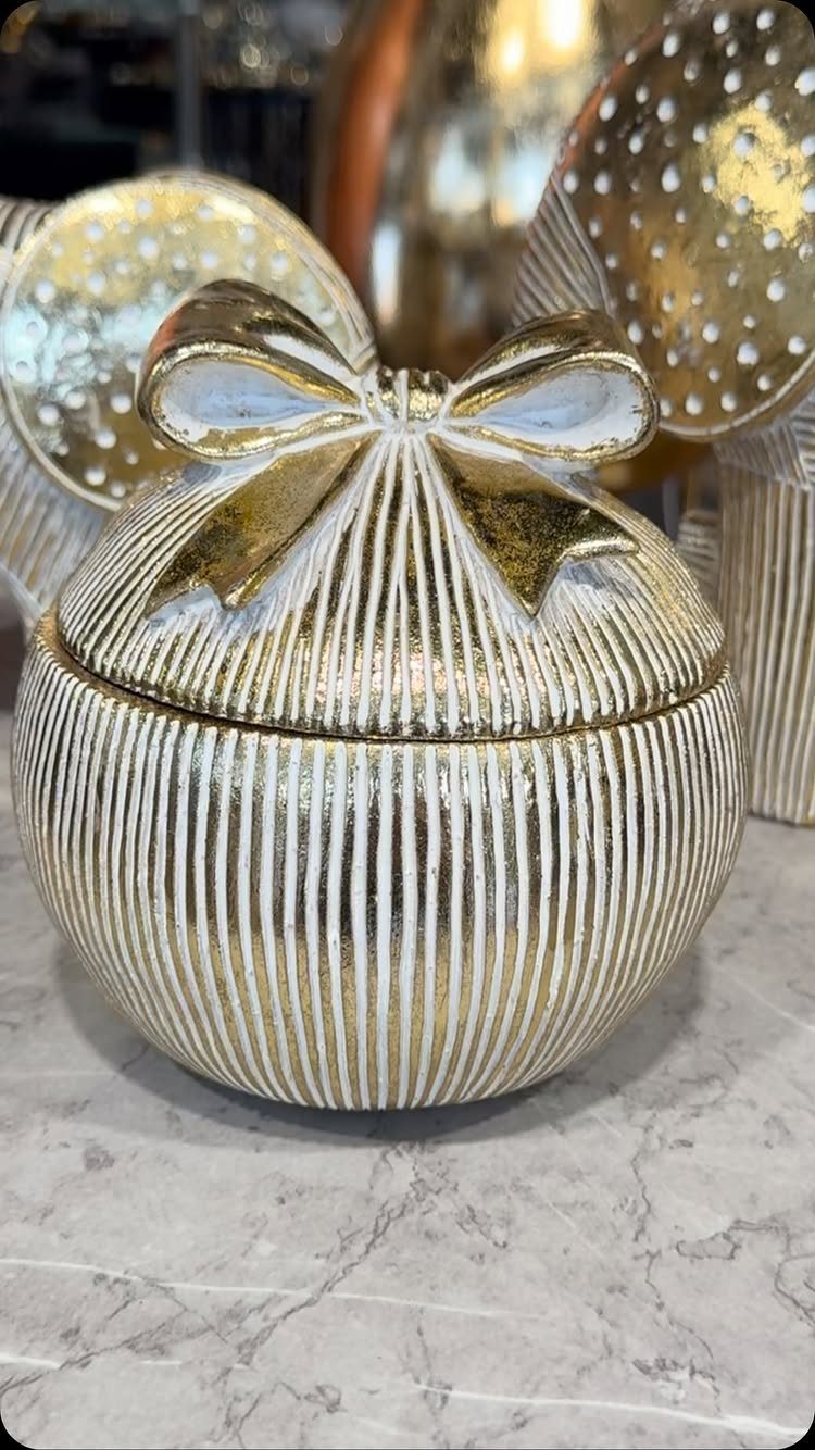 Gold and white striped ceramic gift jar with a bow on marble surface