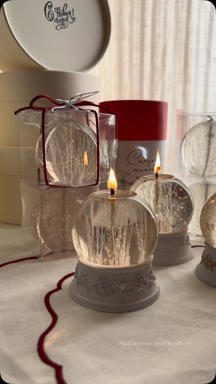 Snow globe candles with lit flames and winter scenes on decorative grey bases.