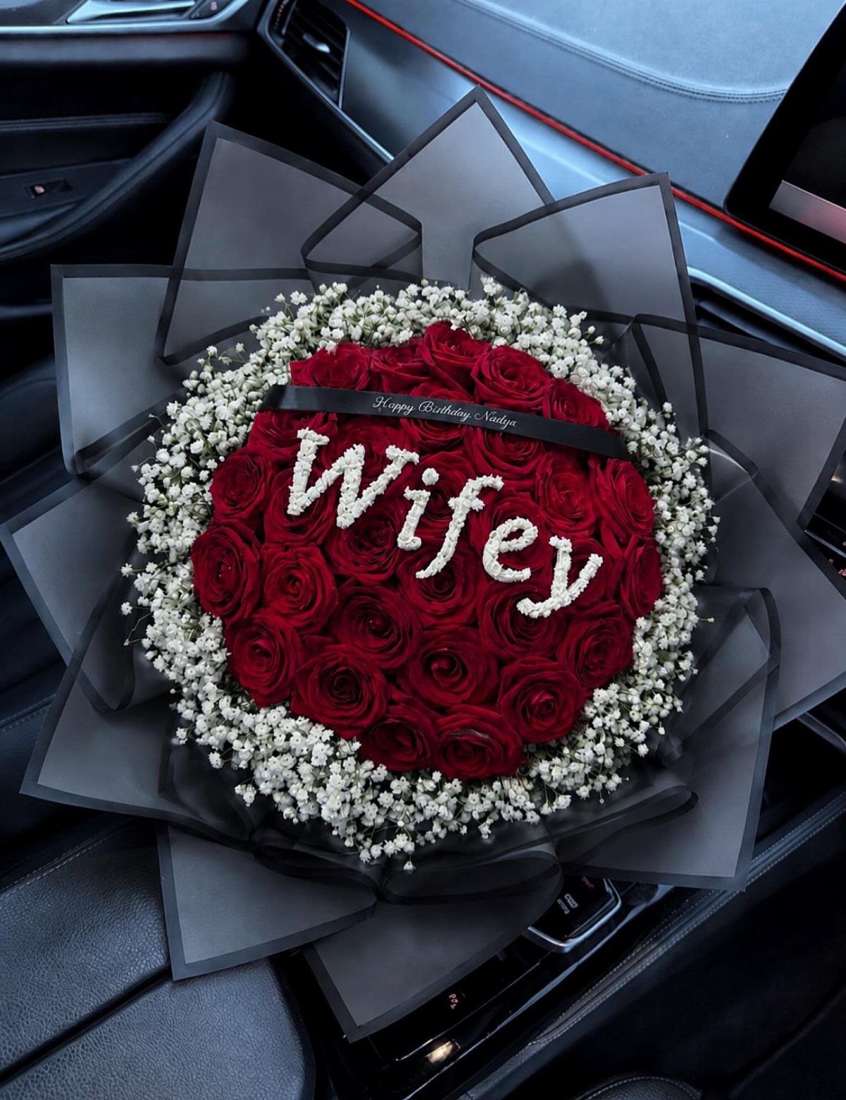 Round bouquet of red roses and baby's breath spelling Wifey in a car