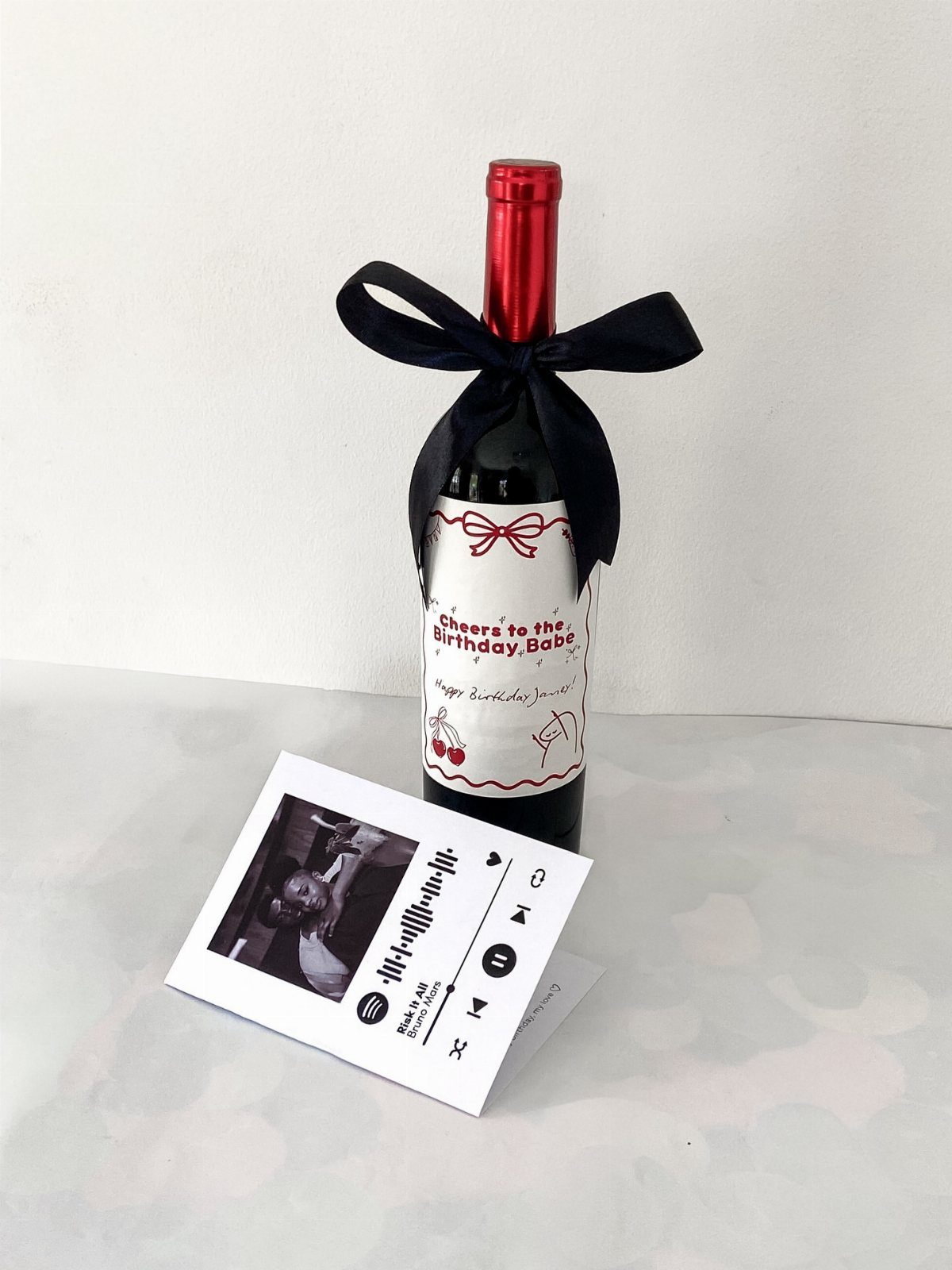Bottle of red wine with a custom birthday label and a black ribbon bow.