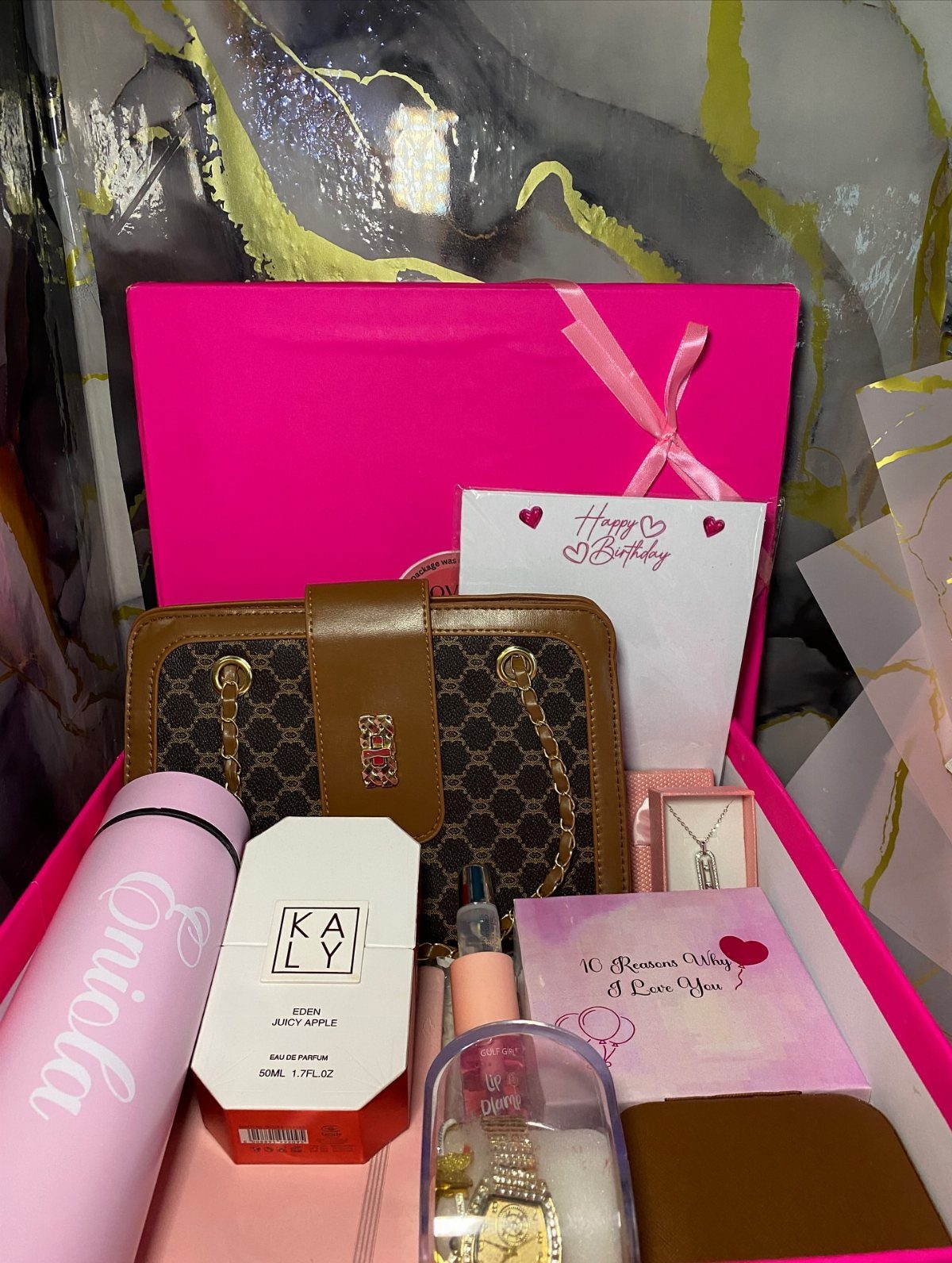 Pink gift box filled with a handbag, jewelry, perfume, and birthday card.
