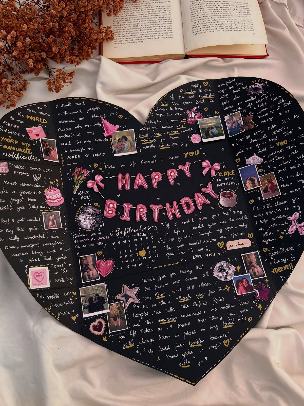 Heart-shaped black birthday board with handwritten messages, photos, and pink decorations.