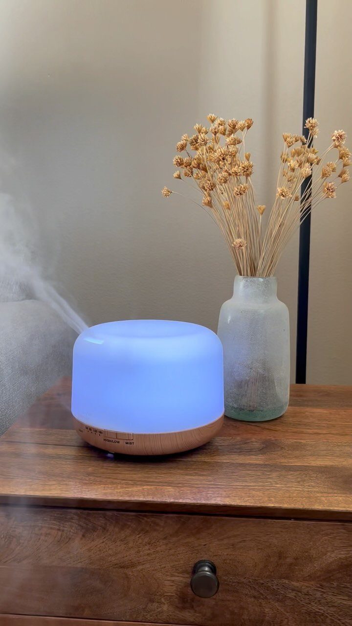 Essential oil diffuser with blue light emitting mist on a wooden dresser