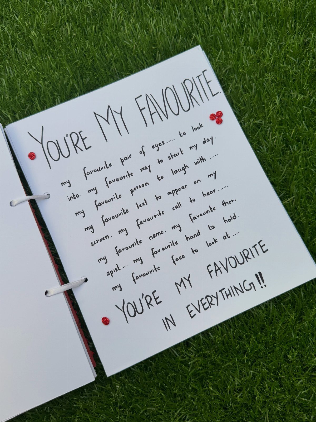Open white notebook with handwritten love letter resting on green grass