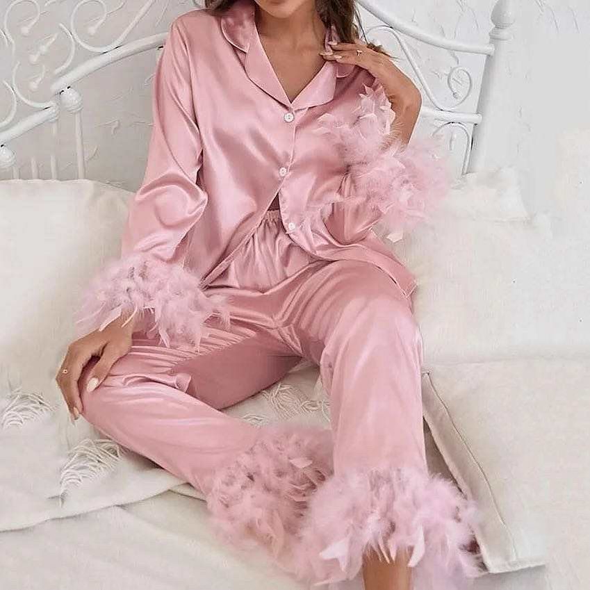 Pink satin pajamas with feather trim worn by a person on a white bed