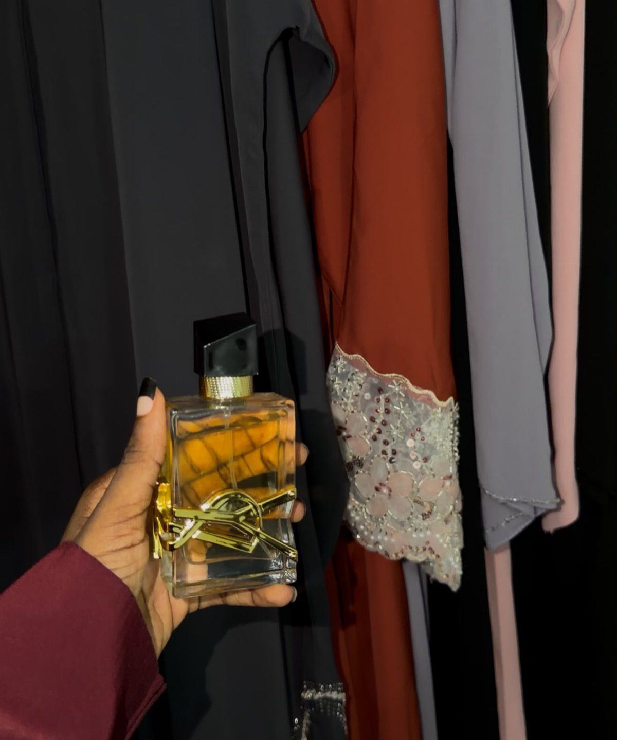 Perfume bottle held in hand against a background of hanging colorful dresses