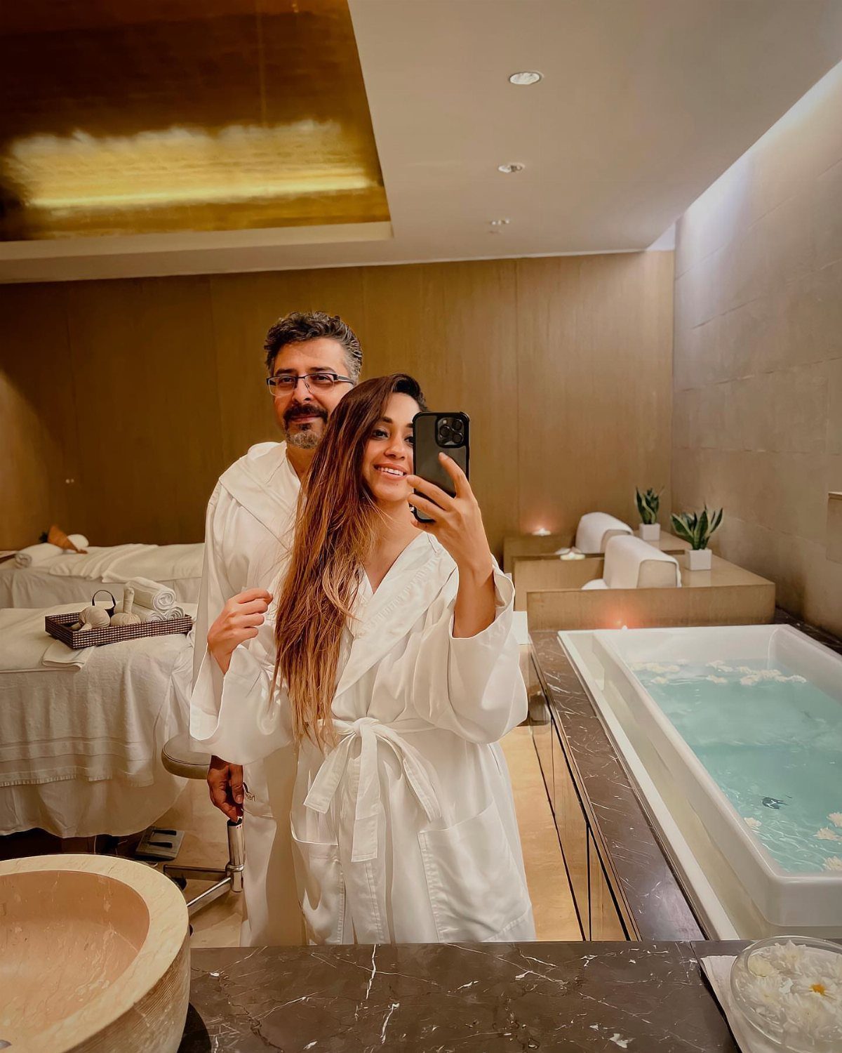 Couple in white robes posing in a luxury spa with a hot tub.