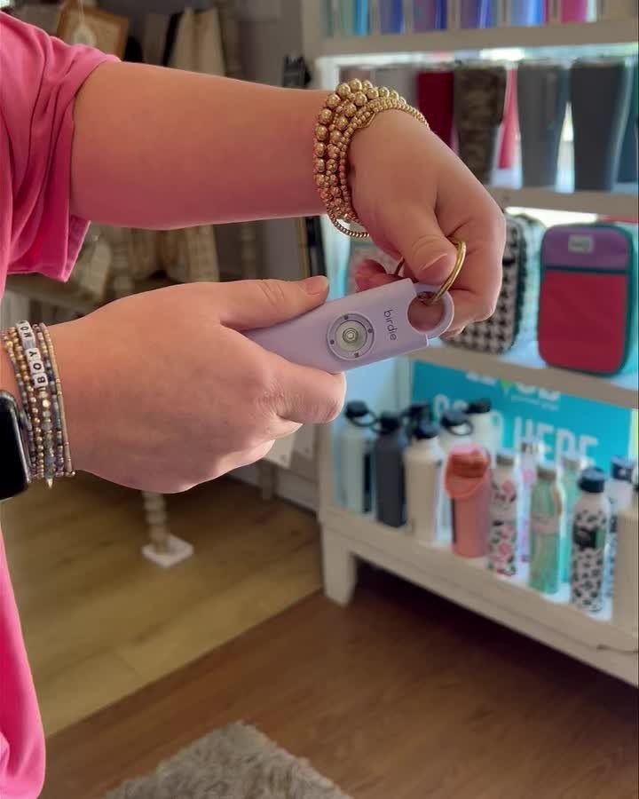 Light purple Birdie personal safety alarm held by a person wearing gold bracelets.