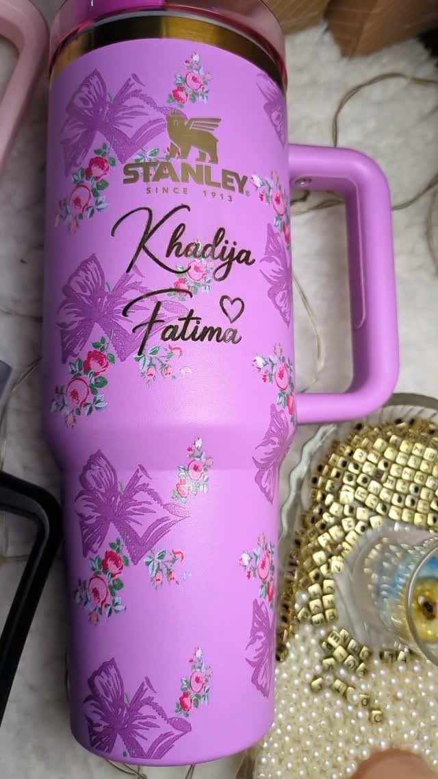 Purple Stanley tumbler decorated with floral patterns, bows, and personalized cursive name.