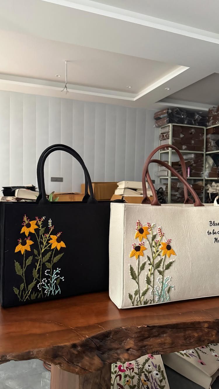 Two tote bags with embroidered yellow sunflowers sitting on a rustic wooden table.