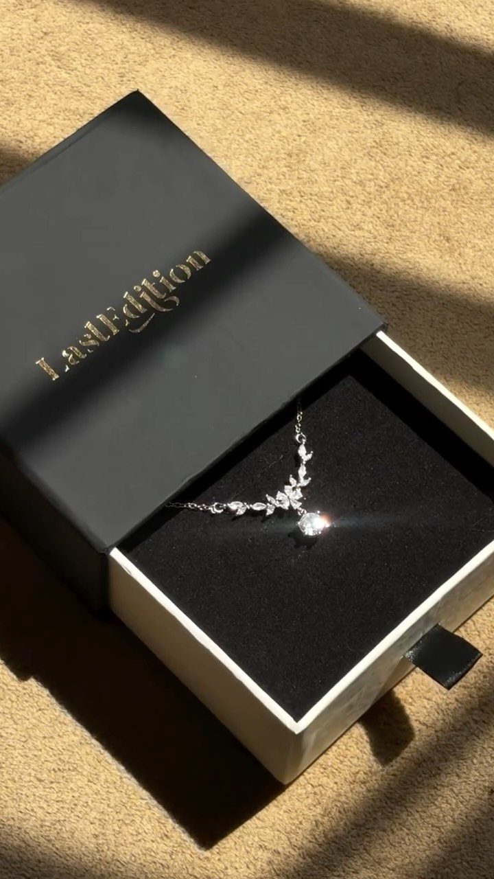 Silver necklace with sparkling pendant in a black velvet jewelry box on beige surface