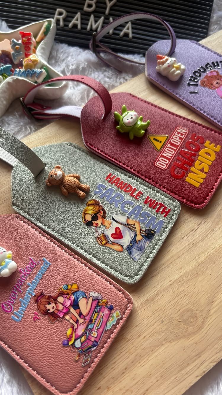 Colorful leather luggage tags with humorous text and cartoon characters on wooden surface