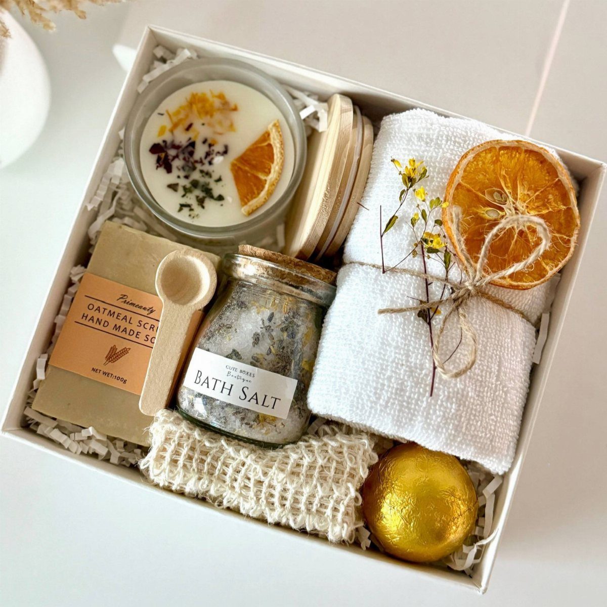 Spa gift box with bath salts, scented candle, oatmeal scrub, and white towel.