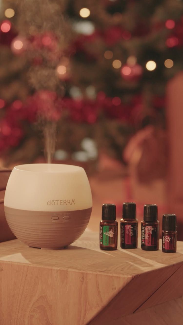 Essential oil diffuser and bottles on a wooden table with blurred Christmas tree background