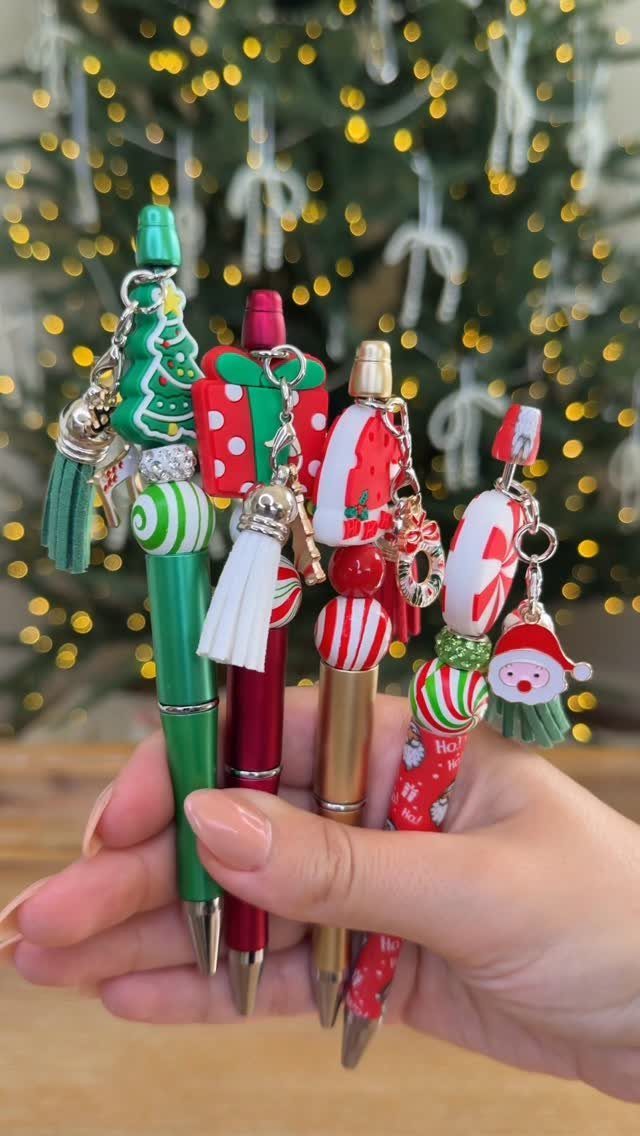 Four decorative Christmas pens with festive charms held in a person's hand.