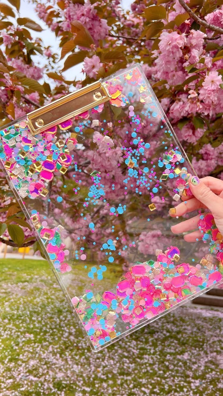 Clear acrylic clipboard with colorful confetti held against pink cherry blossom trees