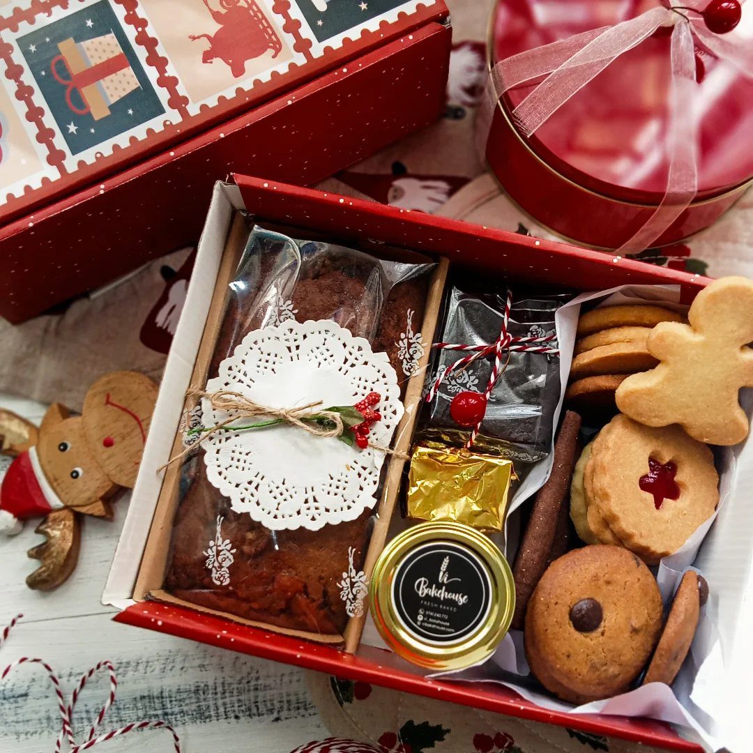 Red gift box filled with a loaf cake, jam, and assorted holiday cookies.