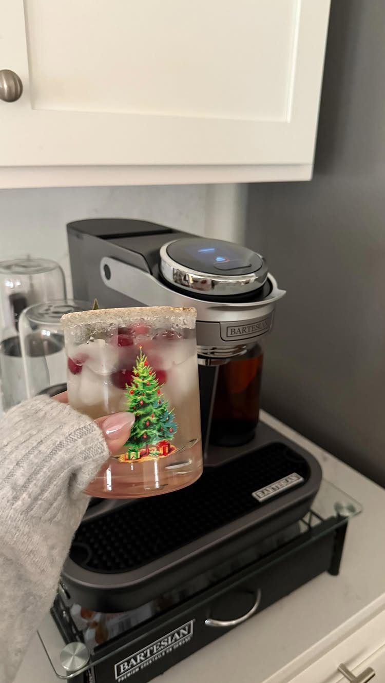 Hand holding a festive cocktail glass in front of a Bartesian cocktail machine.