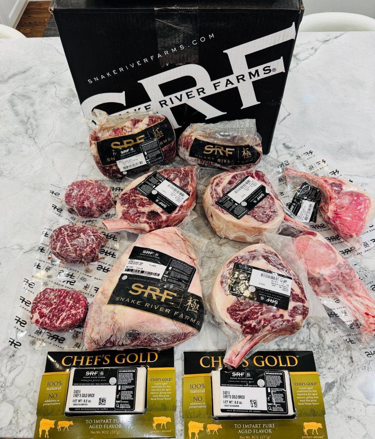 Raw marbled beef steaks in vacuum packaging arranged before a black shipping box.