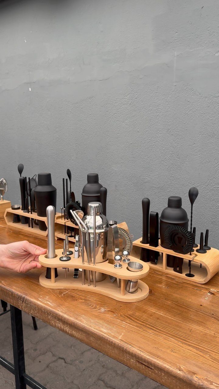 Wooden cocktail shaker set with silver and black bar tools on a table