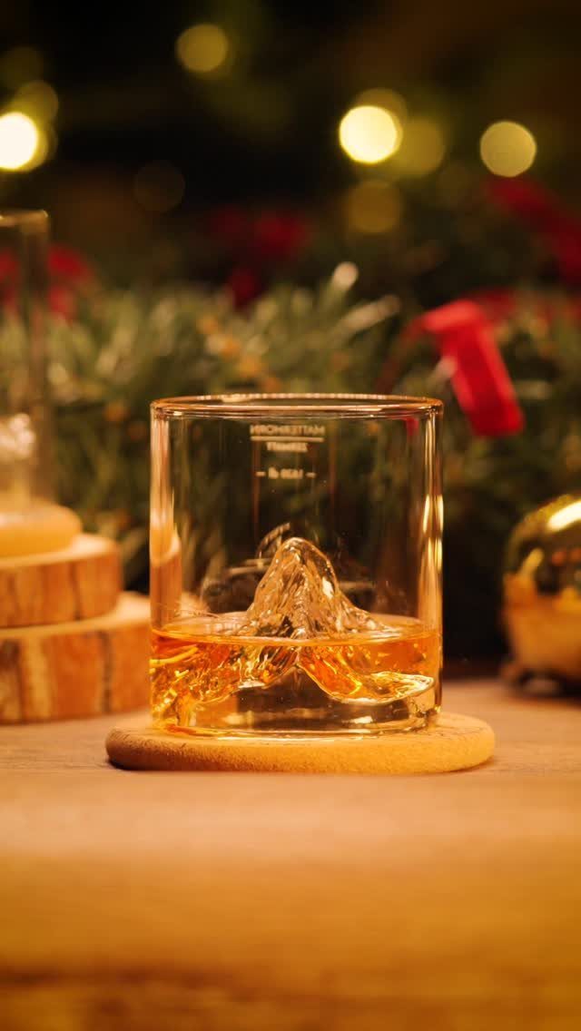 Whiskey glass with mountain ice cube on a wooden coaster with festive lights