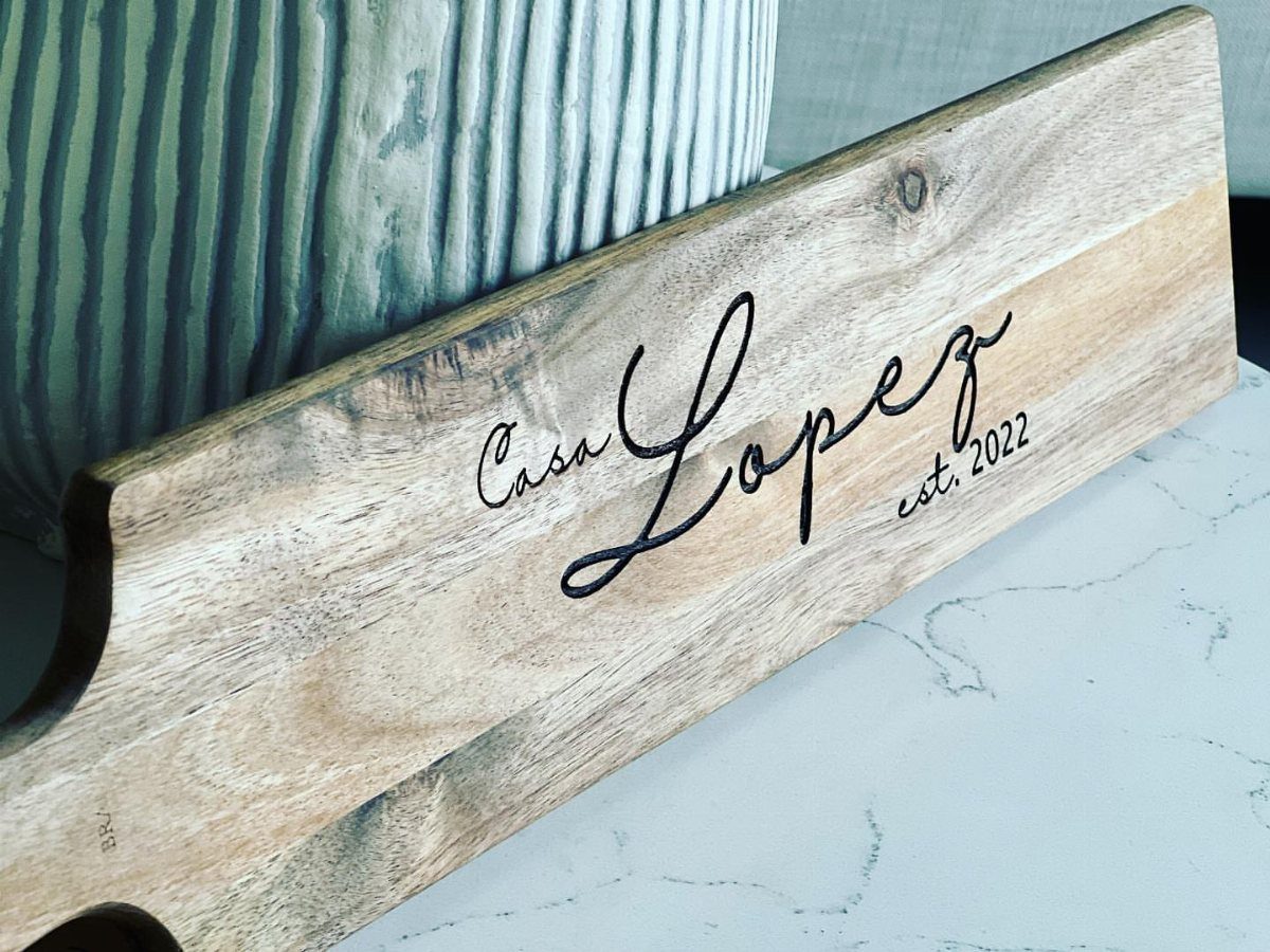Personalized wooden cutting board engraved with Casa Lopez est. 2022 leaning against a vase