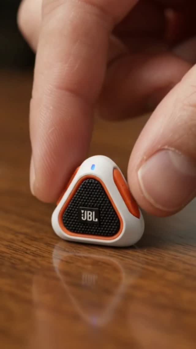 JBL wireless earbud in white and orange held by fingers on wooden table